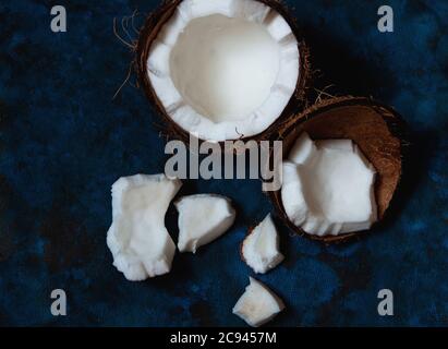 La noix de coco ouverte se trouve sur un fond bleu foncé à côté de morceaux brisés qui se trouvent au hasard Banque D'Images