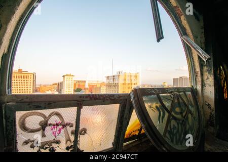 Vue sur une grande et brisée fenêtre voûtée à un City Skyline et Clear Sky dans un bâtiment abandonné Banque D'Images