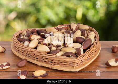 La noix brésilienne, connue sous le nom de 'Castanha do Pará' dans un panier en forme de coeur sur une table en bois avec un fond de jardin non focalisé Banque D'Images