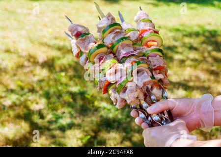 Les mains tiennent le barbecue fait de porc et de légumes sur des brochettes de métal. Banque D'Images