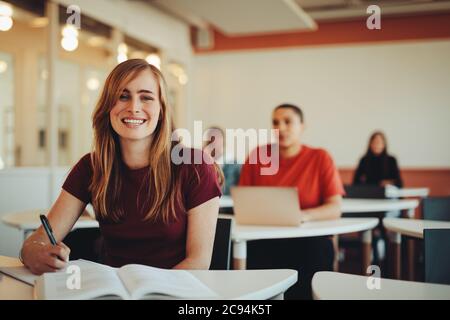 Portrait de l'élève en classe secondaire. Fille dans la salle de classe d'un collègue regardant l'appareil photo et souriant. Banque D'Images