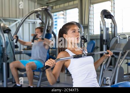 Fitness asiatique femme s'entraîner à tirer l'épaule à la salle de gym. Entraînement de force de fille en utilisant la machine d'extraction de lat Banque D'Images