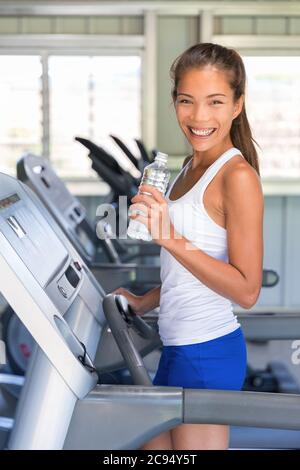 Femme de chemin buvant de l'eau dans la salle de gym. Fille asiatique sur le tapis roulant Banque D'Images