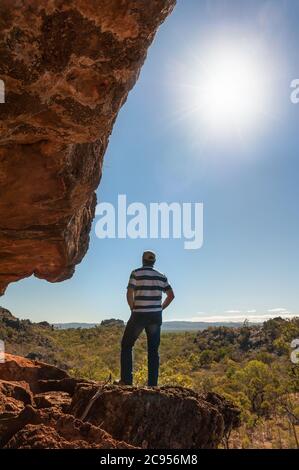 Un randonneur mâle se tient à côté d'une falaise en admirant le soleil couchant sur le pays semi-aride autour de Chillagoe dans l'Outback du Queensland en Australie. Banque D'Images