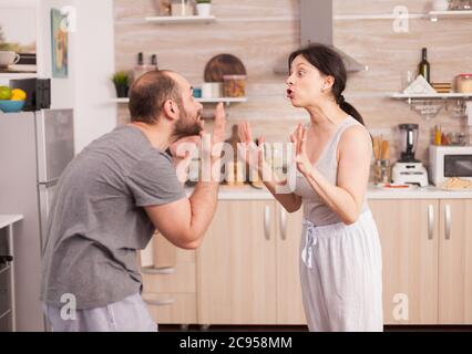 Couple criant les uns aux autres dans la cuisine le matin. Jeunes couples en querelle dans la cuisine. L'homme et la femme hurlent dans la frustration pendant la conversation à domicile. Banque D'Images