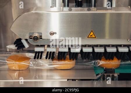 le pain cuit dans un sac en plastique de qualité alimentaire sur le tapis roulant se déplace pour sceller dans la machine d'emballage de la ligne de production de l'usine de fabrication de boulangerie Banque D'Images