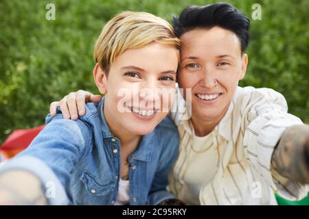 Portrait de deux lesbiennes heureux souriant à l'appareil photo ils prennent le portrait de selfie tout en étant assis à l'extérieur Banque D'Images