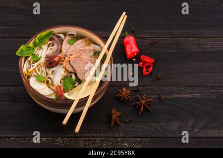 Soupe traditionnelle vietnamienne de pho bo épicée avec nouilles de riz, tranches de bœuf, anis étoilé sur fond de bois brun foncé. Rustique. Banque D'Images