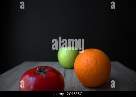 Composition de tomates mûres, de pommes vertes et d'orange sur un panneau de bois sur fond noir Banque D'Images