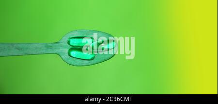 Pilules de gel phosphorescent au néon vert sur une cuillère en bois. Dépendance ou concept de soins de santé Banque D'Images