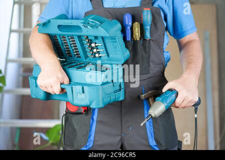 le travailleur tient un tournevis électrique et une boîte à outils dans sa main Banque D'Images