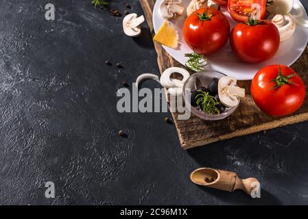 Ingrédients alimentaires et épices pour cuire de délicieuses pizzas italiennes, champignons, tomates, fromage, oignons, poivrons, sel, basilic, olives sur un béton sombre Banque D'Images