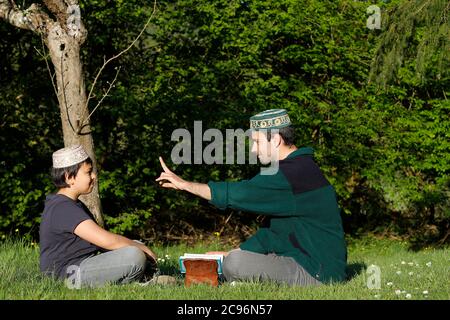 Adolescent et jeune homme lisant le Kuran dans un jardin en France. Banque D'Images