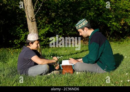 Adolescent et jeune homme lisant le Kuran dans un jardin en France. Banque D'Images