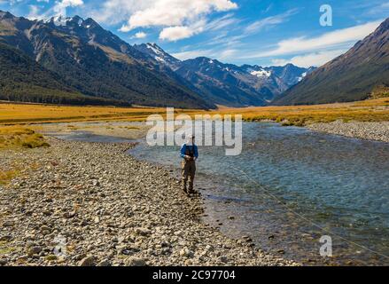 Un pêcheur pêche à la mouche pour la truite sur la rivière Ahuriri, entourée de montagnes dans le bassin MacKenzie, dans l'île du Sud de la Nouvelle-Zélande Banque D'Images