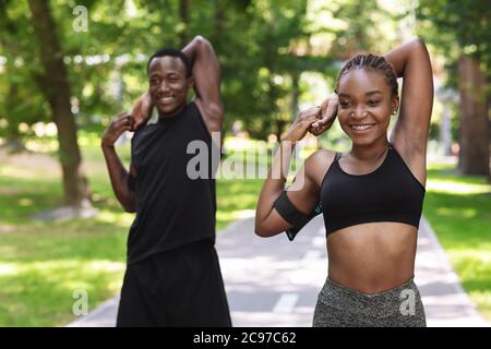 Couple africain sportif s'exerçant avant de faire du jogging au parc, étirant les muscles du bras à l'extérieur Banque D'Images