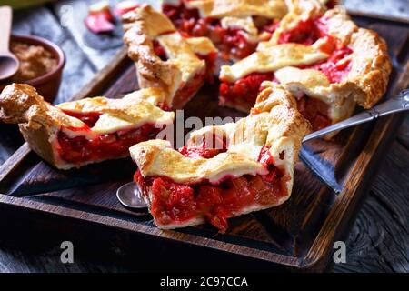 Gros plan de tranches de Rhubarb maison fraîchement cuites aux fraises sur une planche à découper et sur une pelle à gâteau sur une table en bois, Banque D'Images