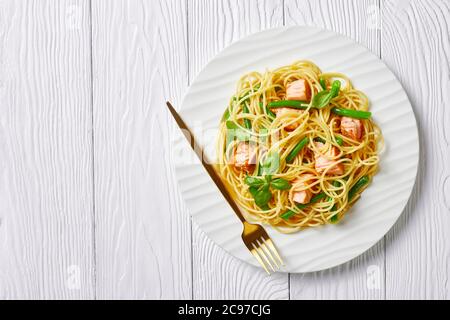 Pâtes au saumon et aux haricots verts avec sauce au beurre à l'ail et basilic frais servies sur une assiette blanche avec fourchette sur fond de bois blanc, vue de Banque D'Images