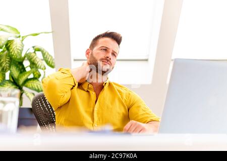 Photo d'un homme d'affaires stressant assis derrière son ordinateur portable et souffrant de maux de tête. Banque D'Images