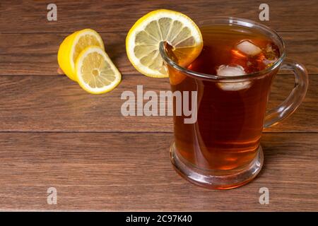 Thé noir avec citron et glace dans un grand mug en verre transparent sur fond de bois brun. Banque D'Images