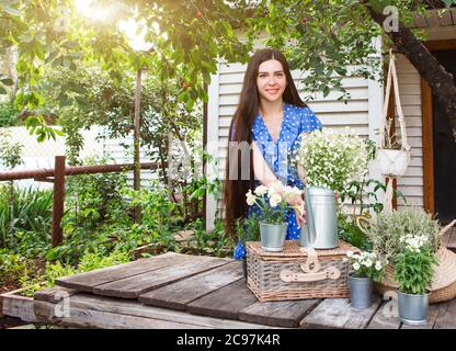 Jeune brunette avec de longs cheveux pot pot avec des fleurs sur le panier sous l'arbre vert le jour ensoleillé d'été dans le jardin Banque D'Images