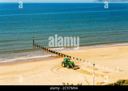 Un tracteur déplaçant du sable sur une plage anglaise par une journée ensoleillée en arrière-plan magnifique océan, industrie côtière Banque D'Images