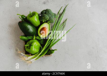 Vue de dessus de divers légumes frais verts placés à l'intérieur du récipient sur fond gris Banque D'Images