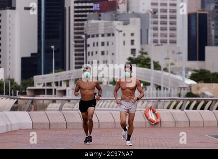 29 juillet 2020, Hong Kong, CHINE : les jeunes hommes font du jogging le long de la promenade du front de mer du port Victoria, au centre, avec des masques chirurgicaux. À la lumière de la nouvelle vague d'épidémie de coronavirus dans la ville, tous les citoyens doivent porter des masques protecteurs à l'extérieur. Les personnes qui s'engagent dans des activités sportives ne sont pas exemptées en vertu du nouveau règlement.juillet-29,2020 Hong Kong.ZUMA/Liau Chung-ren (Credit image: © Liau Chung-ren/ZUMA Wire) Banque D'Images