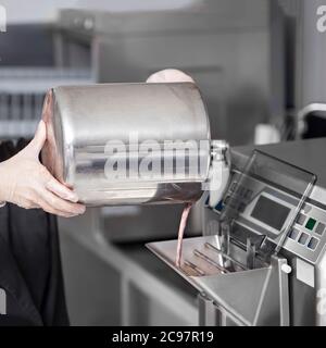 Les femmes font des mains en gants pour préparer de la crème glacée au chocolat - base de lait mélangée dans la machine à crème glacée à la petite fabrication de crème glacée Banque D'Images