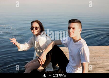 Jeune amie et petit ami heureux sur un quai en bois et regardant les uns les autres tout en appréciant le week-end près du lac Banque D'Images