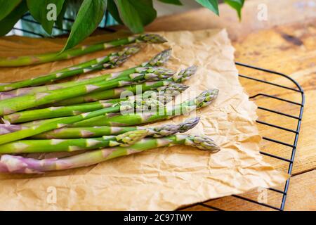 Des asperges vertes fraîches enveloppées dans un emballage en papier brun artisanal pour une cuisine végétarienne saine sur une surface en bois, vue du dessus. Gros plan Banque D'Images