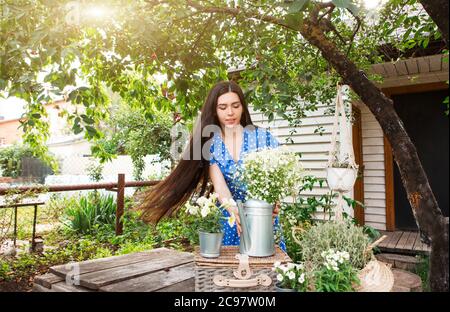 Jeune brunette avec de longs cheveux pot pot avec des fleurs sur le panier sous l'arbre vert le jour ensoleillé d'été dans le jardin Banque D'Images