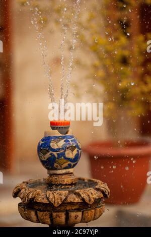 une ancienne fontaine traditionnelle avec un système d'arrosage en plastique contemporain. Gros plan d'une fontaine avec un pot en porcelaine fait à la main avec un rebord brisé. Banque D'Images