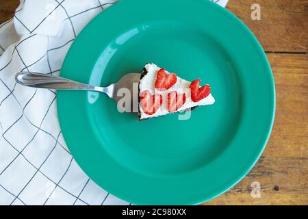 Un cheesecake à la fraise décoré de fraises en forme de coeur se trouve sur une assiette de couleur menthe et repose sur une serviette à carreaux. Vue de abo Banque D'Images