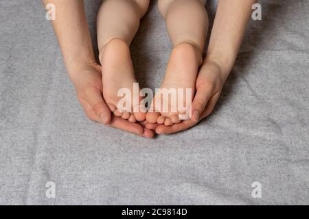 Les jambes des petits enfants, les talons dans les mains parentales affectueuses et douces de la mère. Banque D'Images