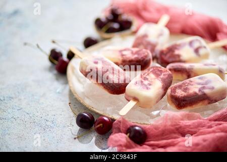 Crème fraîche et cerise des popsicles faits maison placés sur une plaque de céramique blanche avec des fruits et du textile Banque D'Images