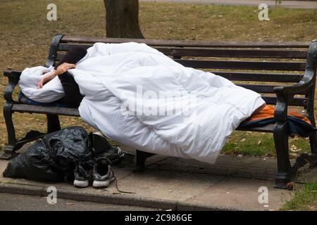 Un homme anonyme et un homme sans abri non identifiable endormi sur un banc de parc dans un espace public. Bournemouth, Angleterre, Royaume-Uni. (120) Banque D'Images