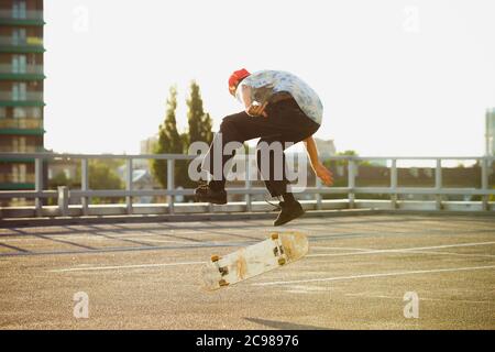 Un skateboarder fait un tour dans la rue de la ville sous le soleil de l'été. Jeune homme en baskets et casquette, équitation et skateboard sur l'asphalte. Concept d'activité de loisirs, sport, extrême, passe-temps et mouvement. Banque D'Images