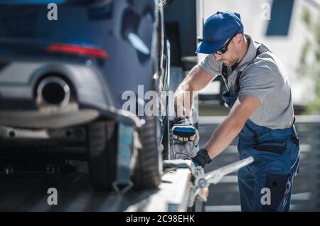 Caucasian Towing Company Worker inn HIS 40s fixer un véhicule moderne sur la plate-forme de remorquage de camion. Transport de voitures. Banque D'Images