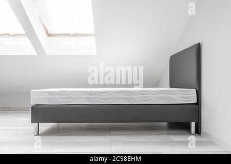 Lit simple dans une chambre d'eau peinte en blanc propre avec fenêtres sur le toit. Intérieur d'appartement simple. Banque D'Images