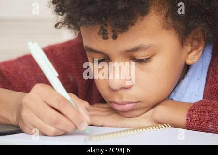 Gros plan d'un garçon africain sérieux se concentrant sur l'étude qu'il est assis à son bureau et faisant de la paperasse Banque D'Images