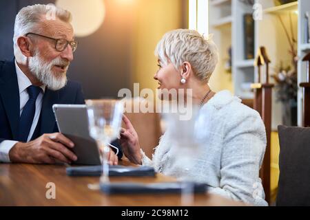 Beau couple senior passant du temps ensemble dans un restaurant riche regarder gadget, sourire, gai Banque D'Images