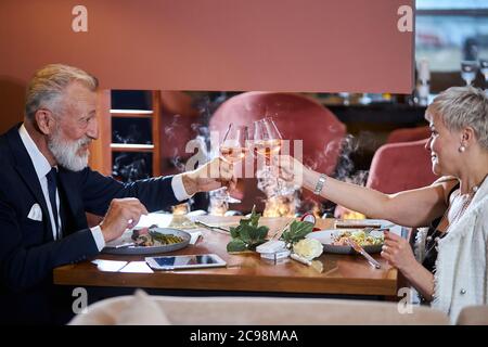 Couple caucasien senior amoureux les uns des autres. Beau homme en costume et femme en verres blancs avec champagne. Fumée légère dans le restaurant. Ros Banque D'Images