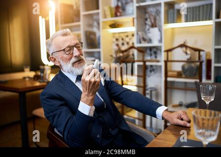 Le vieil homme attrayant aime fumer la cigarette électronique dans le restaurant. Homme senior utilisant e-cigarette, IQOS Banque D'Images