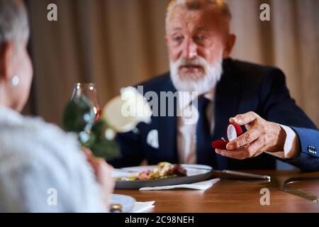 L'homme caucasien à poil gris en tuxedo offre de se marier. Belle visage de l'homme. Femme garder la rose blanche dans les mains Banque D'Images