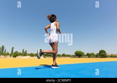 Dos d'une brunette femme sprint sur une piste athlétique. Espace pour le texte. Banque D'Images