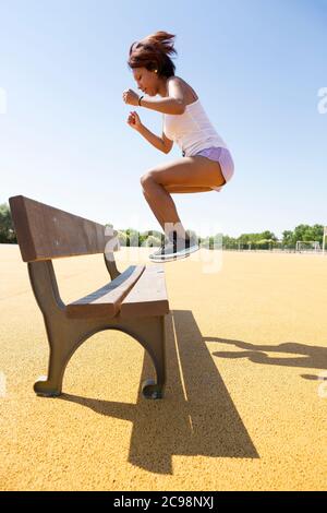 Jeune femme pratiquant des exercices de saut sur un banc extérieur. Elle porte des vêtements de sport. Banque D'Images