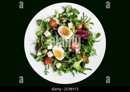 Salade verte saine avec œuf dur, feta, olives, tomates cerises dans une assiette blanche sur fond noir. Flat lay, vue de dessus Banque D'Images