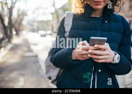 Femme en blouson bleu dans la rue avec un téléphone portable entre ses mains Banque D'Images