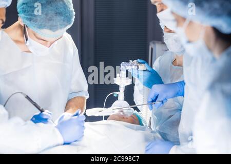 L'équipe chirurgicale concentré l'exploitation d'un patient dans une salle d'opération. Anesthésiste bien formés avec des années d'entraînement avec des machines complexes fol Banque D'Images